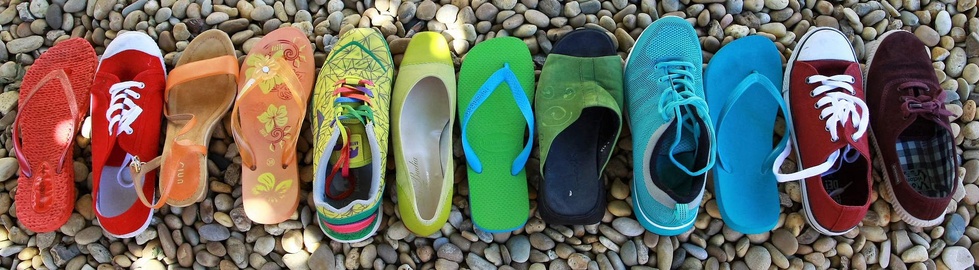 An assortment of shoes laid out in rainbow order on grey stones.
