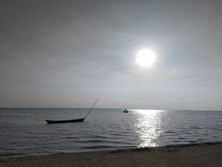 Sun reflecting in the river. Some small boats are driving in the distance, one mooring by the beach.