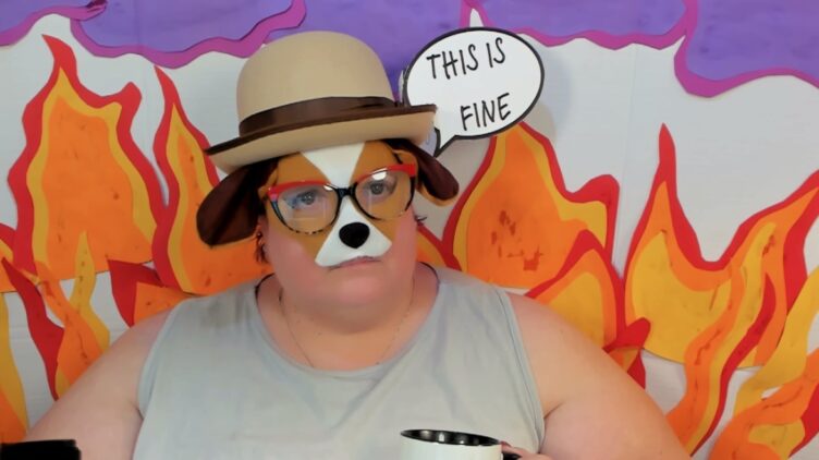 Michelle, dressed as the dog from the "This is Fine" meme with a bowler hat, dog mask, and flames simulated behind her.