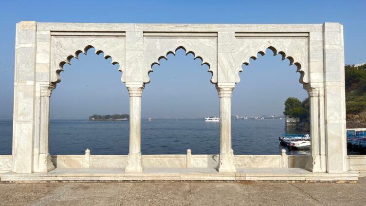 Big marble gate structure at the bank of the lake with docked boats and a distant island in the background.