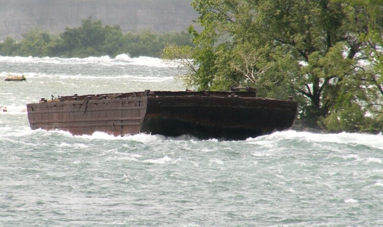 The Niagara Scow, caught on rocks, surrounded by white water rapids and a tree.