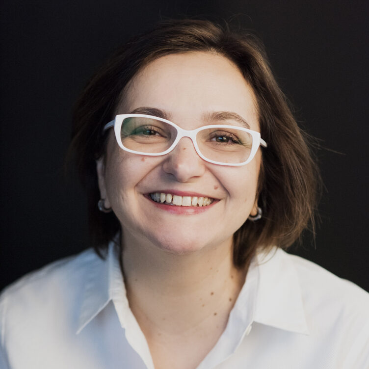 Francesca Marano's headshot. She is a white woman with shoulder length brown hair, a bit smile, brown eyes, and white glasses. She is wearing a white collar shirt.