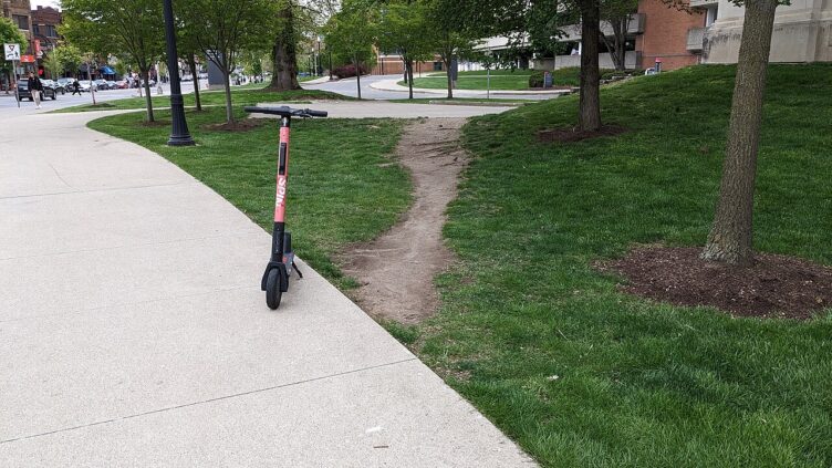 A worn desire path shortcuts across a lawn shortening the distance that would be achieved by staying on the sidewalk.