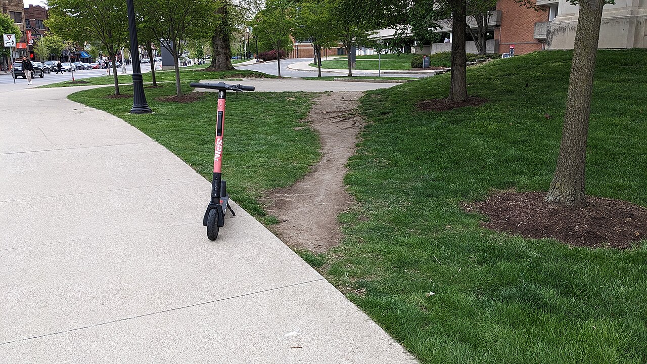 A worn footpath shortcut across a lawn shortening the distance that would be achieved by staying on the sidewalk.